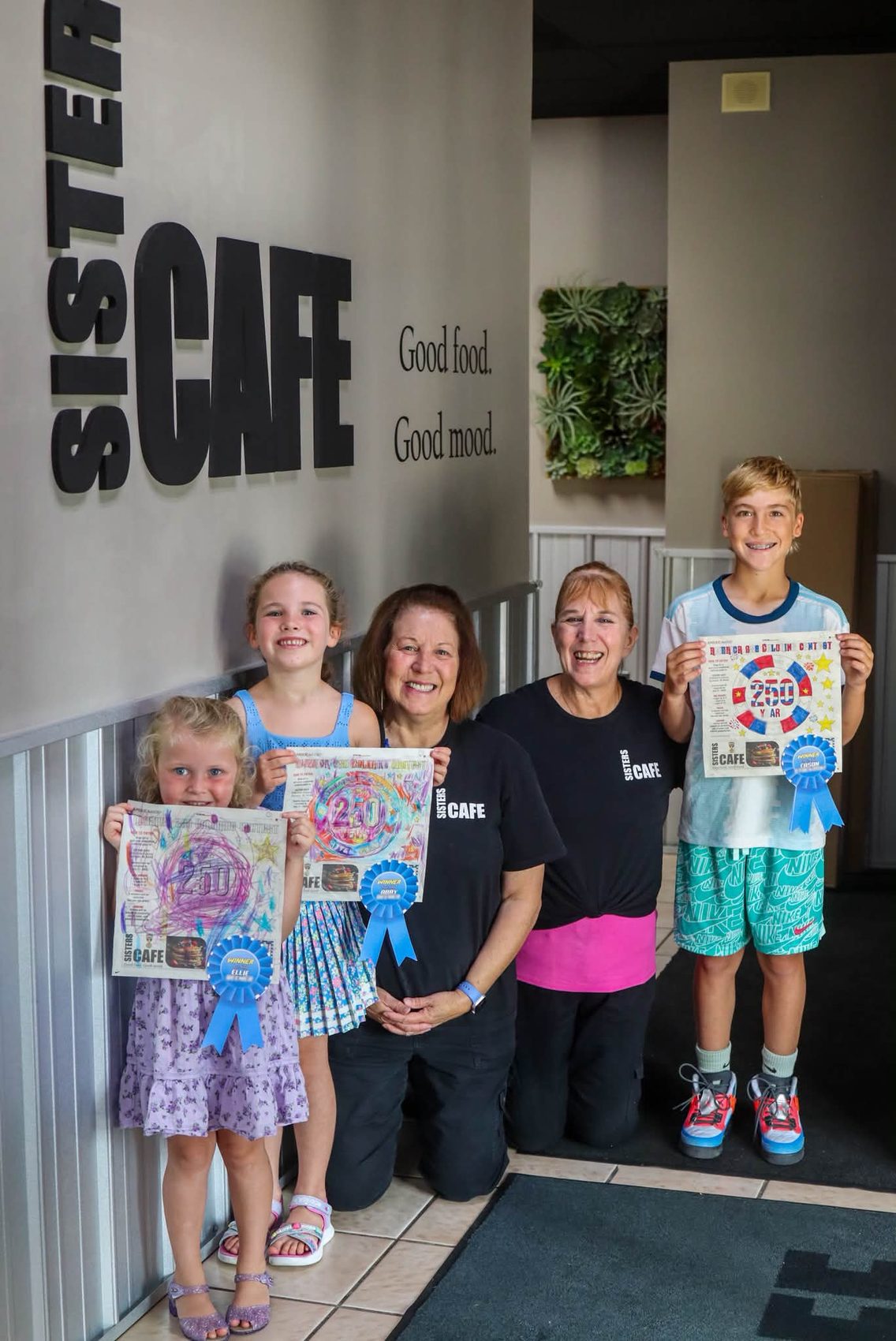 Coloring contest winners holding their prize baskets and ribbons with staff at the cafe