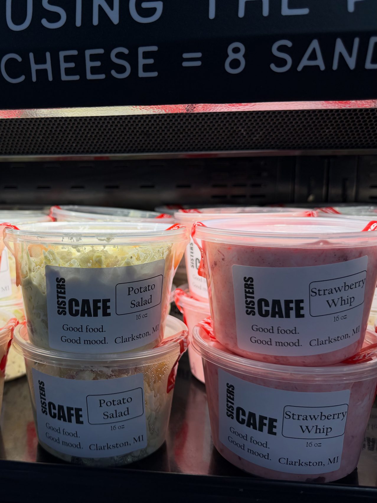 Sisters Cafe branded containers of potato salad and strawberry whip in the deli case at Meijer