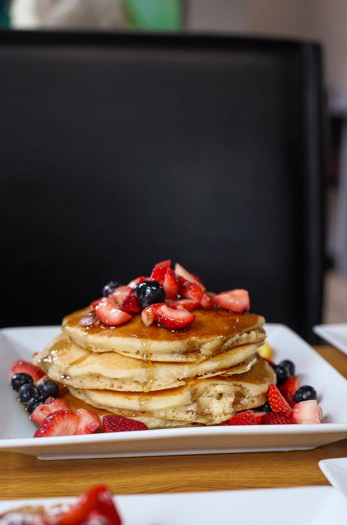 A tall stack of pancakes topped with fresh strawberries and mixed berries at Sisters Cafe